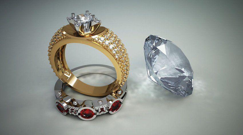 Gold and platinum diamond rings beside a loose diamond